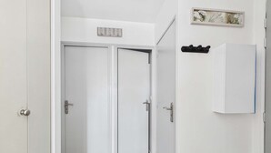Un pasillo con puertas blancas, un interruptor de luz y un pequeño estante con un cuadro.