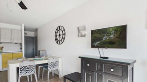 Una cocina moderna con armarios blancos, una mesa de comedor con sillas, un reloj, un televisor y un mueble con cajones.