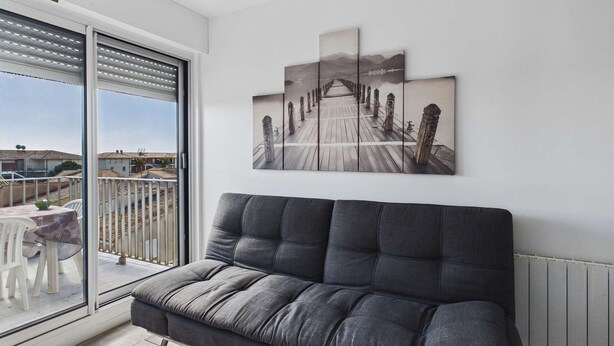 Una sala de estar moderna con un sofá gris, un ventanal con persianas y una obra de arte con múltiples paneles en la pared.