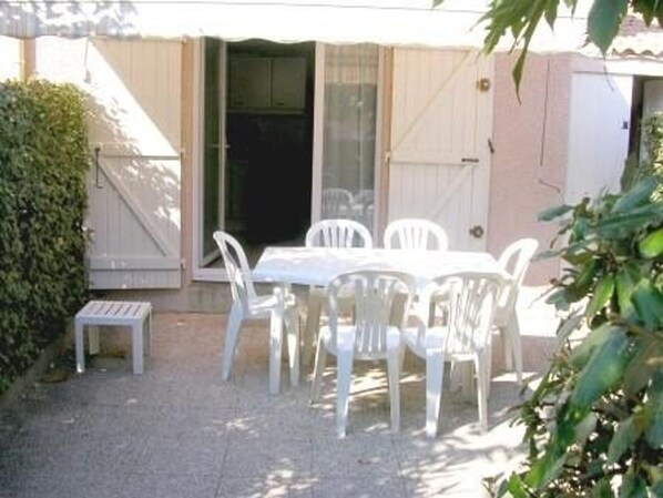 A patio with a white table and chairs, a small bench, and a sliding glass door.