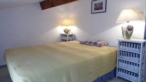 A bedroom with a bed, two bedside tables with lamps, a wall-mounted picture, and a white bedside cabinet. - Modern 2-Bedroom Townhouse with Terrace, Private Parking & Pool Access in Marseillan (Marseillan-Plage)