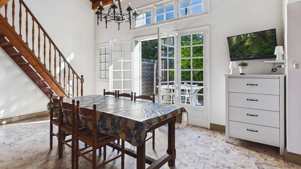 A dining area with a wooden table and chairs, a chandelier, a television on a cabinet, and a staircase. - Spacious house 70m from the sea, Le Grau d'Agde (Le Grau d'Agde)