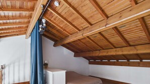 A small, single-room attic bedroom with a sloped wooden ceiling, a bed, a white dresser, and a window with blue curtains. - Spacious house 70m from the sea, Le Grau d'Agde (Le Grau d'Agde)