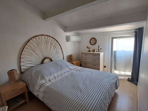 A bedroom with a bed, a dresser, a nightstand, a wall-mounted air conditioner, and a window with curtains.