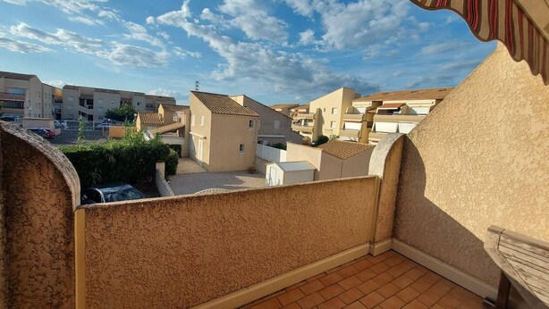 Un balcón con vistas a edificios residenciales, suelo de baldosas y un toldo a rayas.