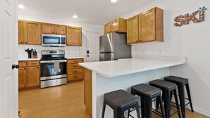 Una cocina moderna con armarios de madera, electrodomésticos de acero inoxidable, una isla blanca con taburetes altos y un cartel con la palabra 'SKI' en la pared.