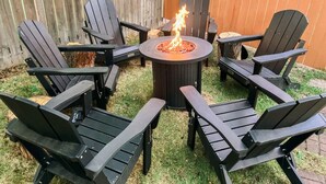 Un área de estar al aire libre circular con un brasero en el centro, rodeada por seis sillas Adirondack.
