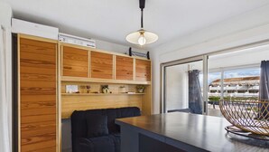 A modern kitchen with a wooden cabinet, a black sofa, and a large window. - Cozy Studio Apartment with Pool Access near Beach in Marseillan, Sleeps 4 (Marseillan-Plage)