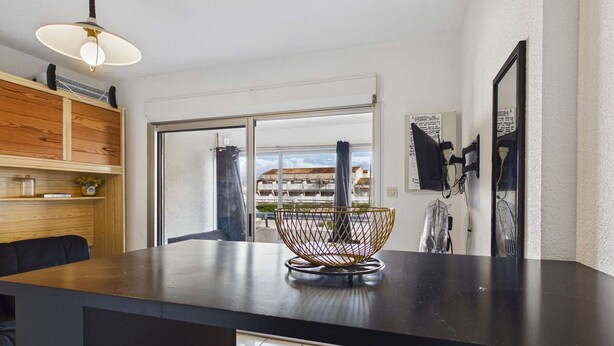 A modern kitchen with a black countertop, wooden shelving, and a large window with a view of buildings. - Cozy Studio Apartment with Pool Access near Beach in Marseillan, Sleeps 4 (Marseillan-Plage)