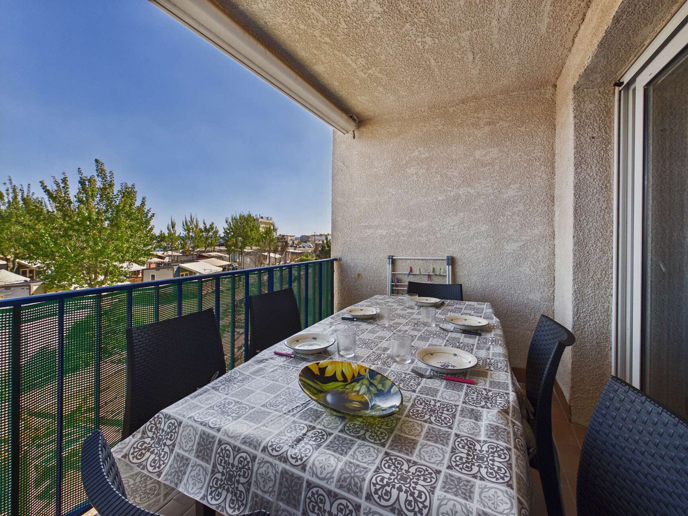 A balcony with a table set for dining, chairs, and a view of the cityscape.