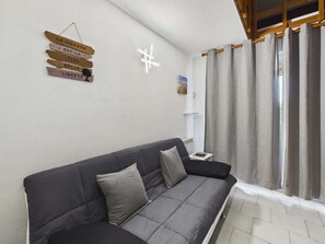 A modern living room with a dark grey sofa, a small table with a lamp, and a wall-mounted sign with French phrases.