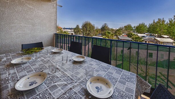 A balcony with a table set for dining, a view of the sea, and a green fence. - Charming Studio with Mezzanine & Terrace for 6 in Marseillan, Parking Included (Marseillan-Plage)