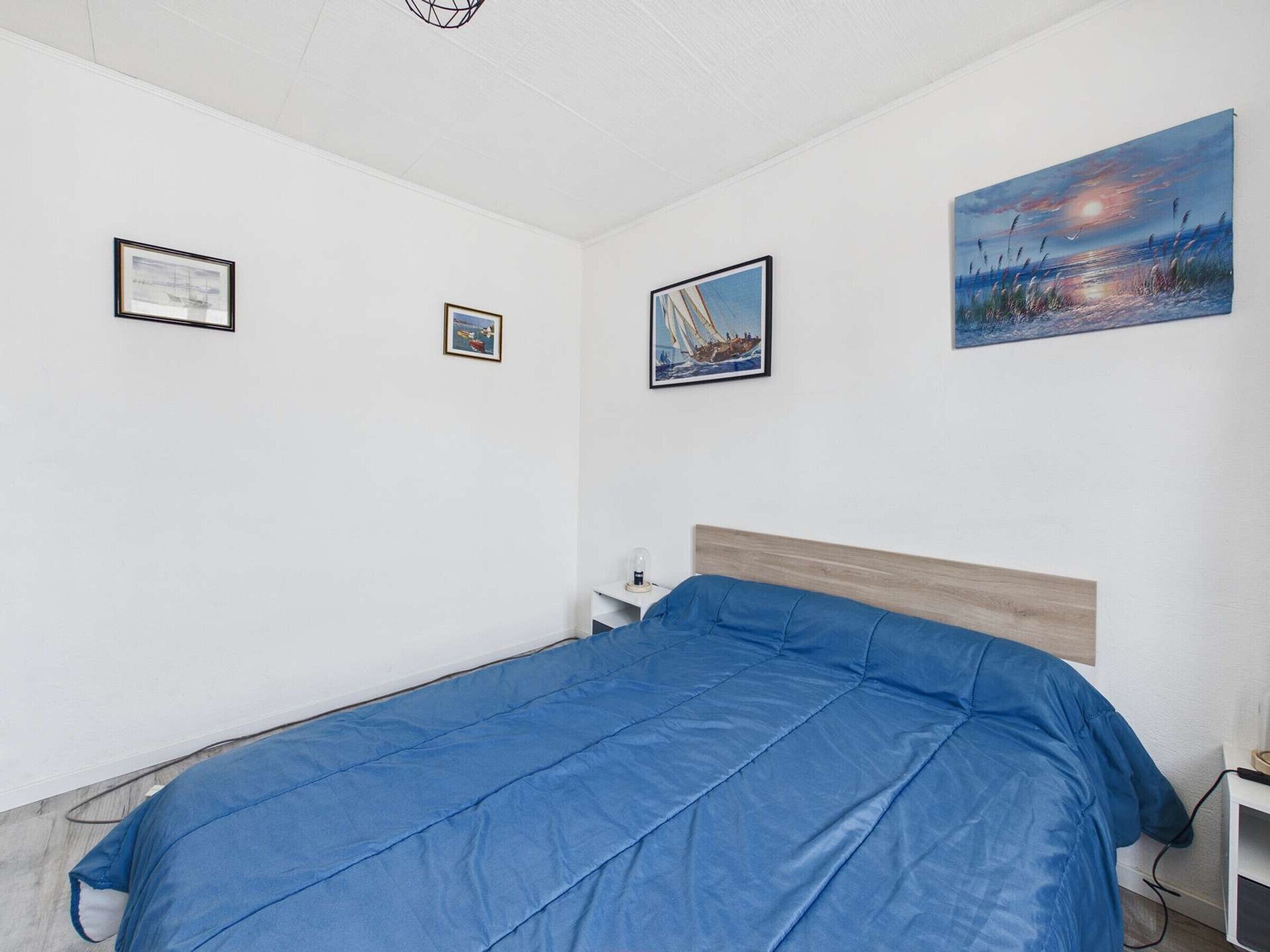 Een slaapkamer met een bed, nachtkastje, lamp en drie ingelijste foto's aan de muur.