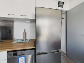 A stainless steel refrigerator in a kitchen with white cabinets and a wooden countertop.