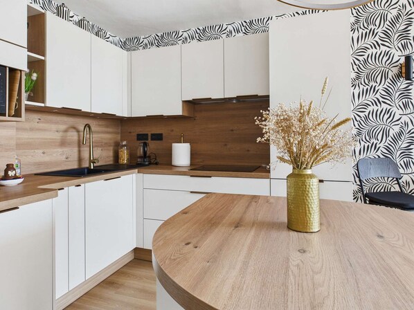 A modern kitchen with white cabinets, a wooden countertop, a round dining table, and a vase with dried flowers.