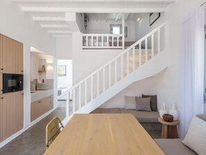 Un intérieur moderne avec une table à manger en bois, un escalier avec des rampes blanches et un coin cuisine doté de meubles en bois.