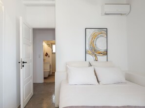 Une chambre d’hôtel avec un lit, une salle de bain visible à travers une porte ouverte et un climatiseur fixé au mur.