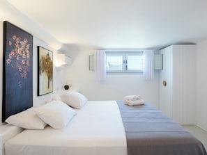 Une chambre d’hôtel comprenant un lit, une table de chevet, une lampe fixée au mur, une fenêtre avec des rideaux et une armoire.