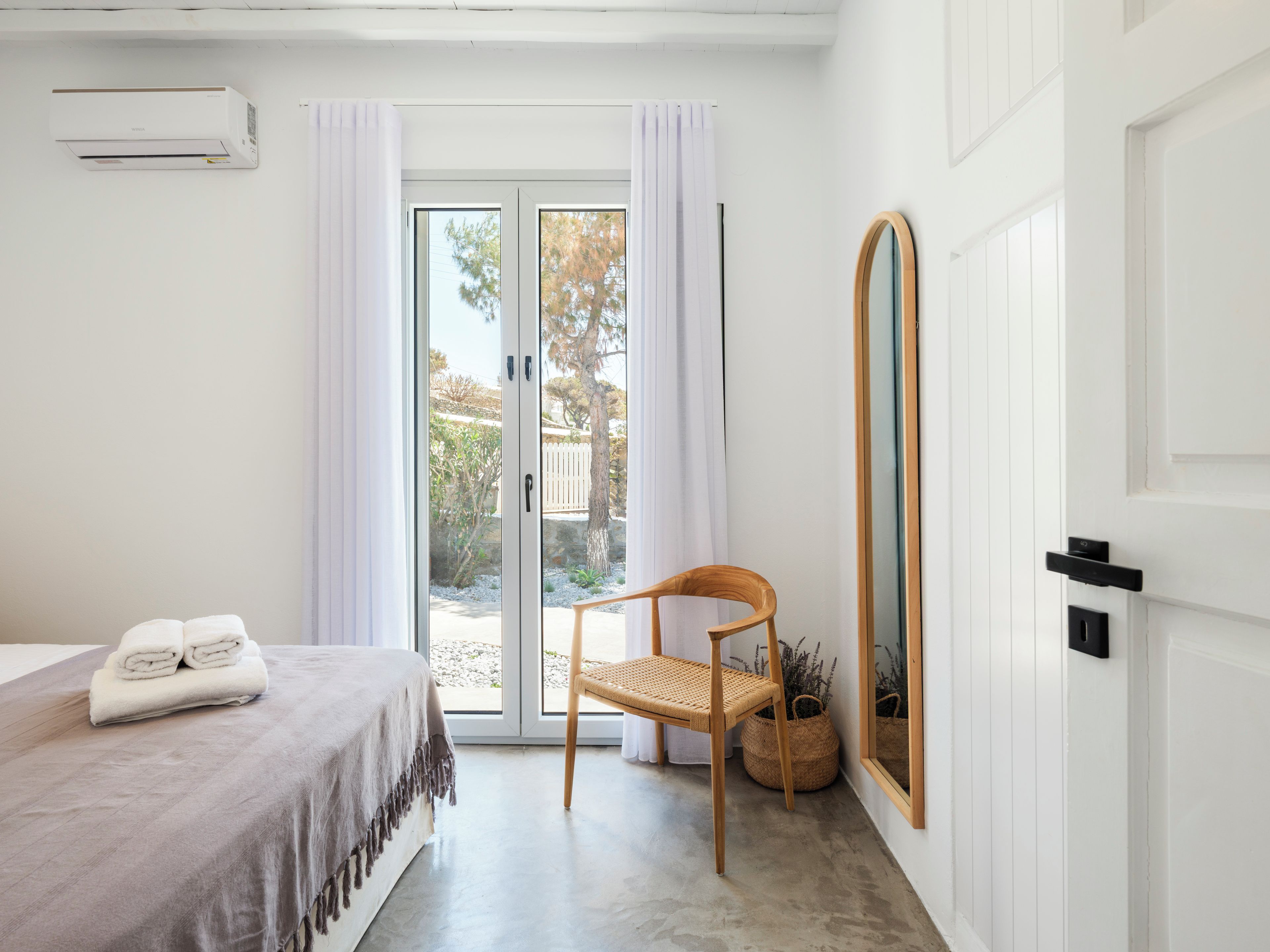 Une chambre à coucher comprenant un lit, une chaise, un miroir et une porte-fenêtre coulissante donnant sur un espace extérieur.