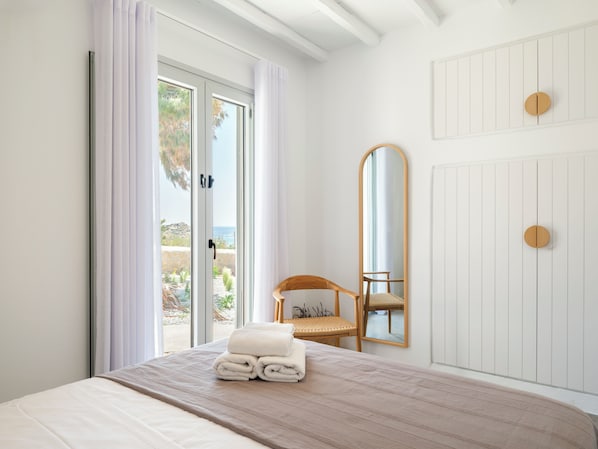 Une chambre à coucher avec un lit, une chaise, un miroir et une vue sur l’extérieur.