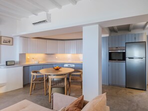 A modern kitchen with a built-in oven, a stainless steel refrigerator, and a dining area with a round table and chairs.