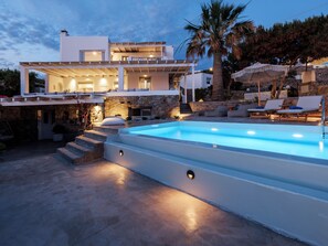 Une maison moderne dotée d’une piscine, d’un espace salon extérieur et d’un mur en pierre.