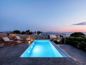 Une piscine avec des chaises longues et une vue sur la mer au crépuscule.