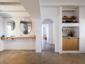Un intérieur moderne comprenant un espace cuisine, un couloir menant à une autre pièce et un meuble en bois doté d’étagères.