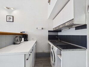 Una cocina compacta con lavadora, cafetera y hervidor sobre la encimera.