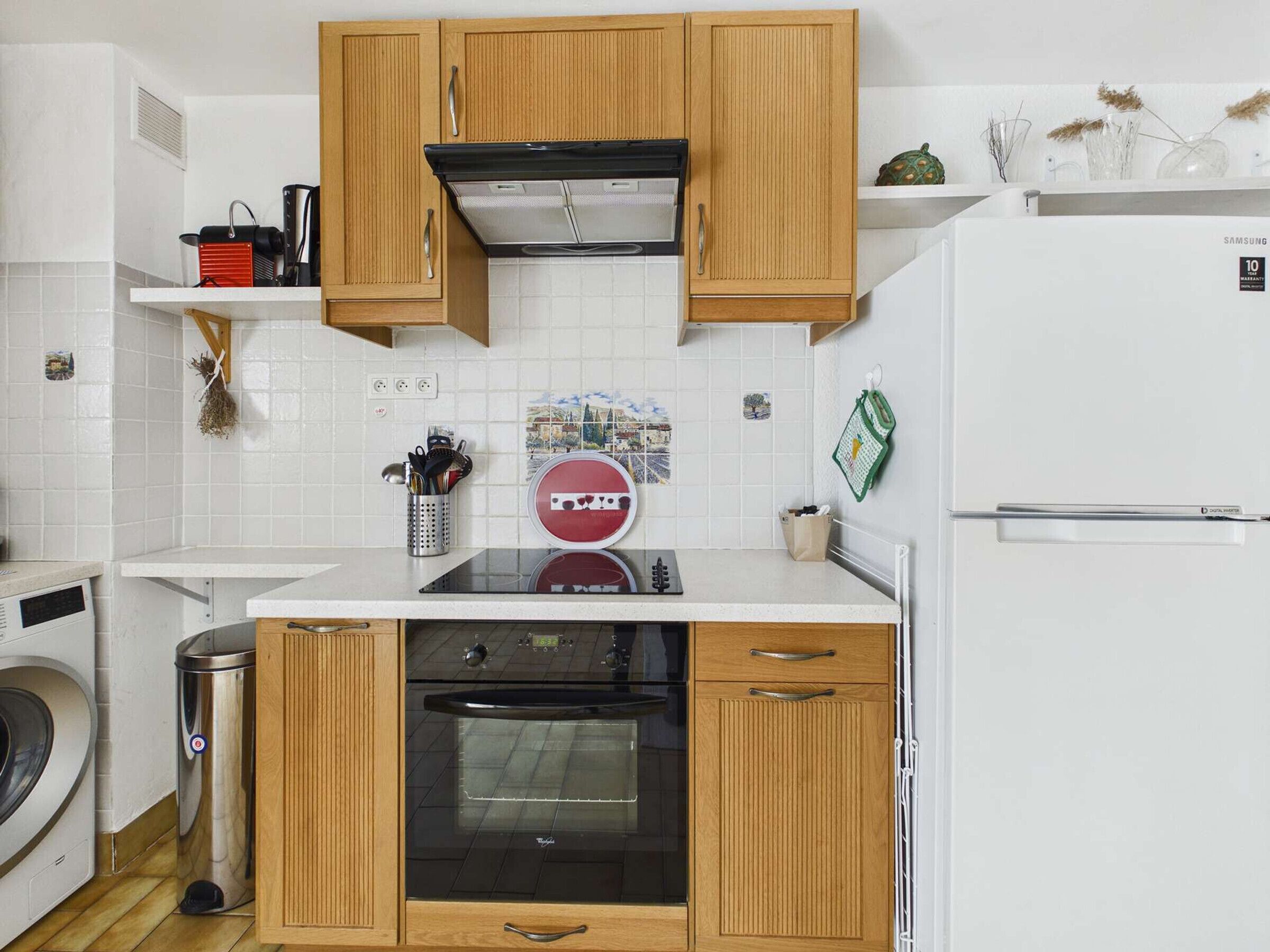 A compact kitchen with wooden cabinets, a built-in oven, a stainless steel trash bin, and a white countertop.