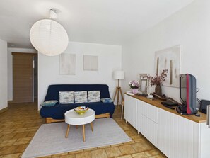 Un salon moderne comprenant un canapé, une petite table ronde, une lampe et un bureau avec un ordinateur et d’autres objets.