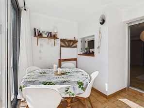 A dining area with a table set for four, a bookshelf, a wall-mounted light, and a window with curtains.