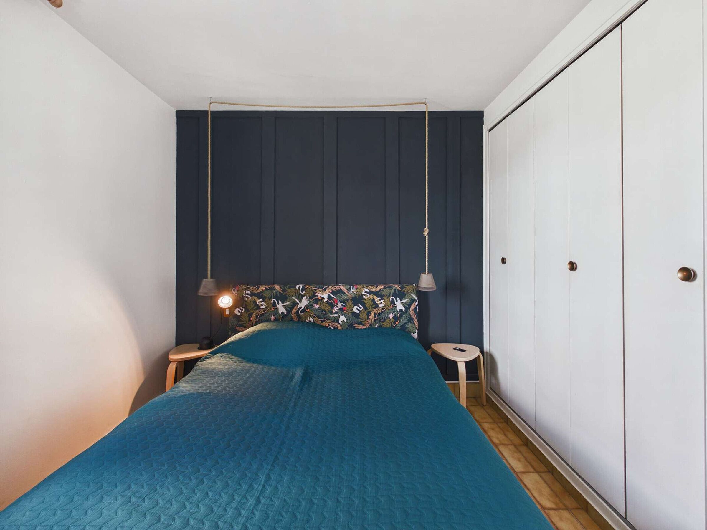 Une chambre à coucher comprenant un lit, une table de chevet, une lampe suspendue et une armoire.