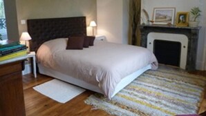 A bedroom with a bed, bedside lamps, a fireplace, and a small table with books.