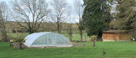 A greenhouse in a grassy field with trees in the background.