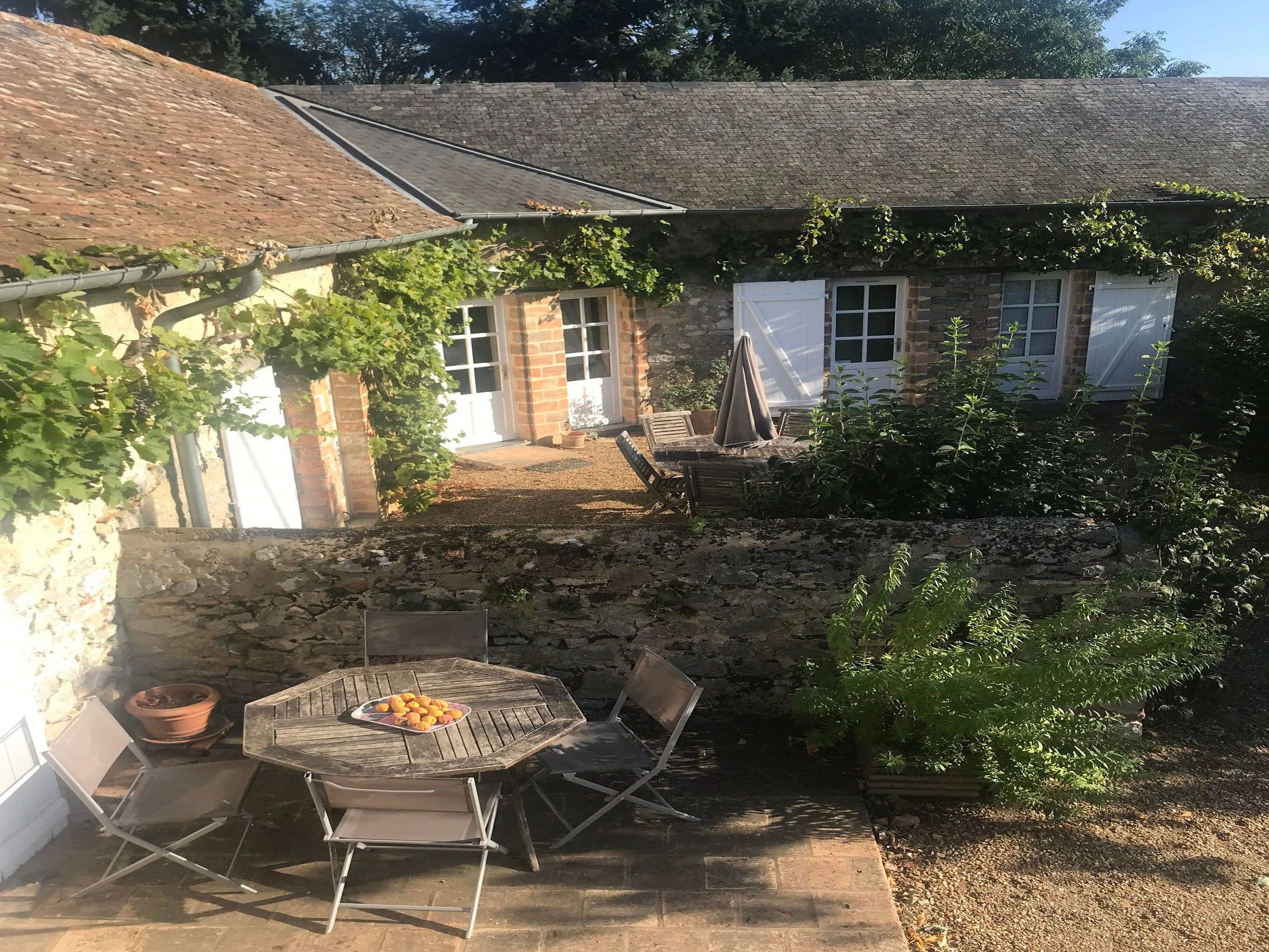 Une terrasse en pierre avec une table ronde et des chaises, un pot de fleurs et un petit jardin agrémenté d’un muret en pierre.