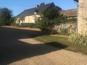 A house with a gravel driveway, a stone wall, and a garden with various plants. - Charming Country Guesthouse with Pool near Solesmes Abbey (Solesmes)