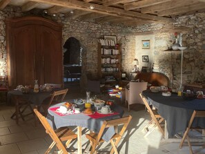 A dining area with stone walls, wooden furniture, and a bookshelf. - Charming Country Guesthouse with Pool near Solesmes Abbey (Solesmes)