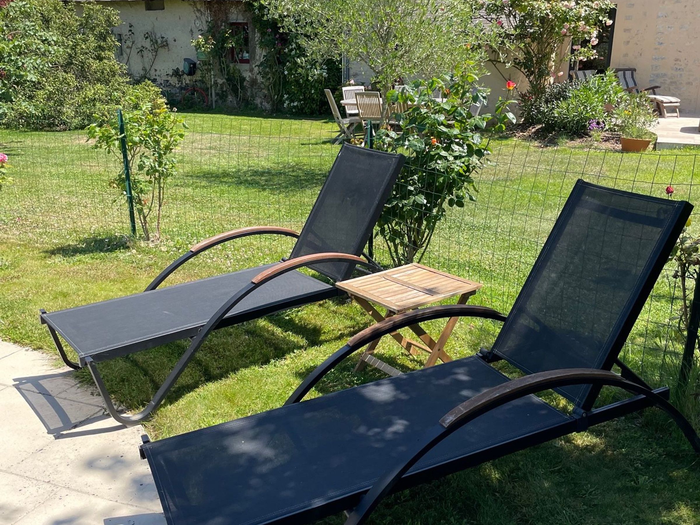 Een tuin met twee loungesteunen en een klein houten tafeltje.