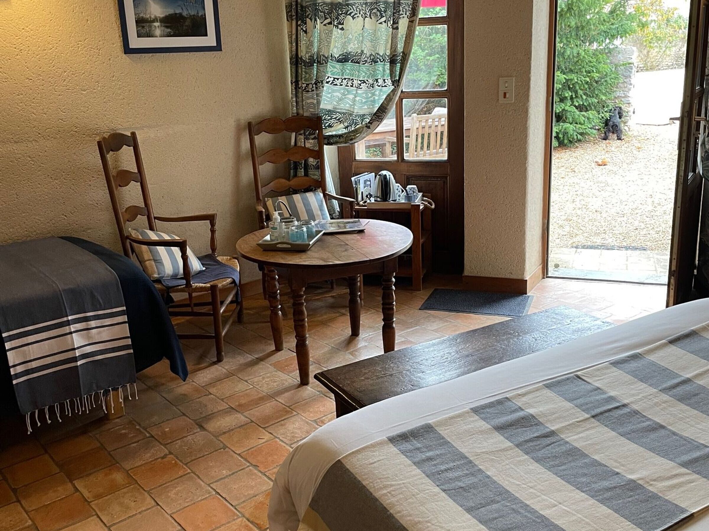 Ein gemütliches Zimmer mit Bett, Sessel, einem kleinen Tisch mit Tablett und einem Fenster mit Vorhängen.