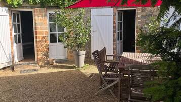 Un espace patio avec une table et des chaises, une plante en pot et un parasol rouge.