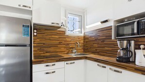 A compact kitchen with a stainless steel refrigerator, a microwave, a coffee maker, and a sink with wooden backsplash.