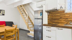 A compact kitchen with a built-in refrigerator, wooden staircase, and a dining area with a table and chairs.