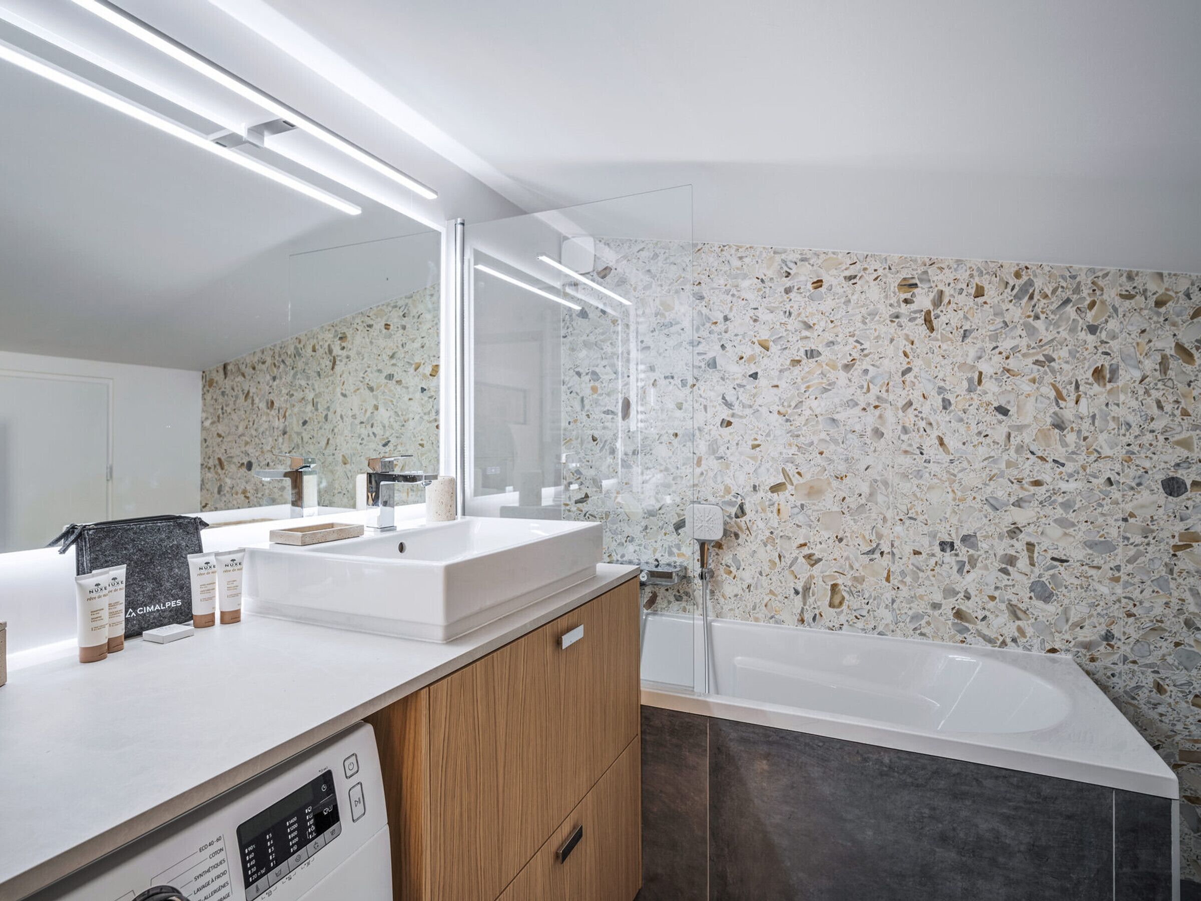 A modern bathroom with a white sink, mirror, and a bathtub with a terrazzo floor.