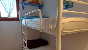 A bunk bed room with a window, a shelf with books, and a painting on the wall.