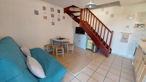 A living room with a blue sofa, a small table with chairs, a wooden staircase, and a kitchen area.