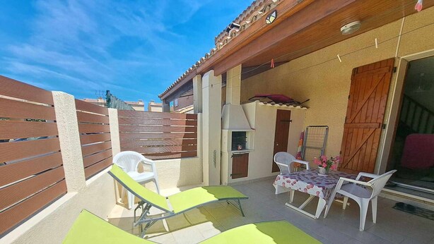 An outdoor patio area with a wooden pergola, a barbecue grill, and a table with chairs.