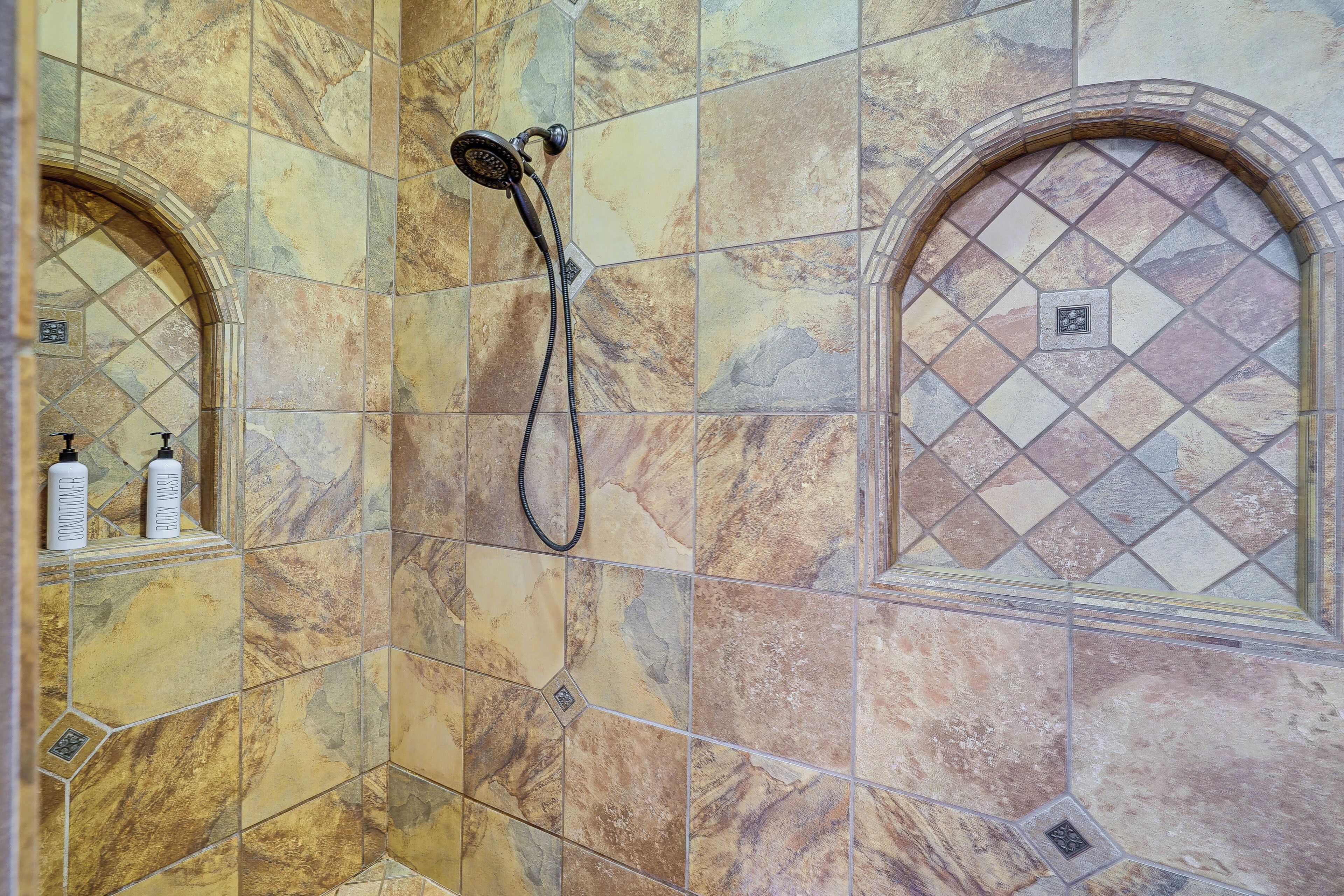Un baño con ducha, paredes de azulejos y dos botellas en un estante.