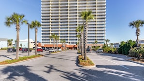 A hotel parking lot with palm trees and a large building in the background. - Gulf Shores Beachfront Condo w/ Community Pool! (Gulf Shores)
