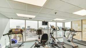 A gym with treadmills, ellipticals, and a stationary bike, large windows with a view of buildings, and a ceiling with recessed lighting. - Gulf Shores Beachfront Condo w/ Community Pool! (Gulf Shores)